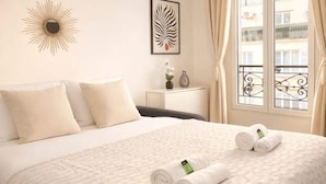 A hotel room with a bed, pillows, a sunburst wall decoration, a framed leaf artwork, a vase with flowers, and a window with curtains. - Cozy apartment in the heart of Paris (Paris)