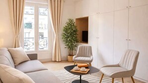 A modern living room with a sofa, two chairs, a coffee table, a potted plant, a TV, and a wardrobe. - Cozy apartment in the heart of Paris (Paris)