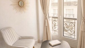 A room with a white chair, a round table, a book, and a sunburst mirror on the wall. - Cozy apartment in the heart of Paris (Paris)