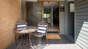 Un espace patio avec une table en métal et deux chaises, une porte-fenêtre coulissante et un paillasson.