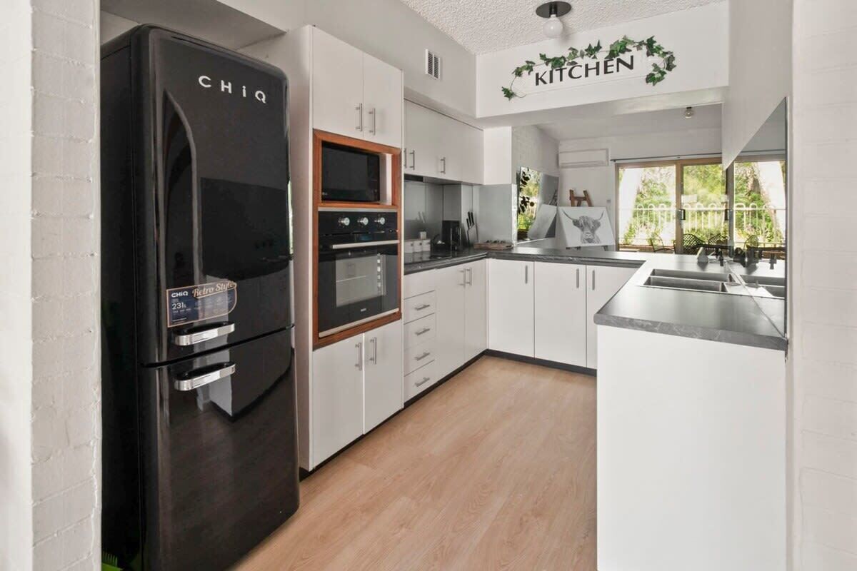 A modern kitchen with white cabinets, a black refrigerator, and a built-in oven.