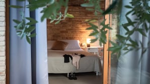 Ein Schlafzimmer mit Ziegelwand, einem Bett mit weißer Bettdecke, einem Nachttisch mit Lampe und einem Fenster mit Vorhängen.