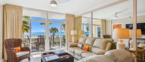 A spacious living room with a large window, a ceiling fan, and a view of the ocean.