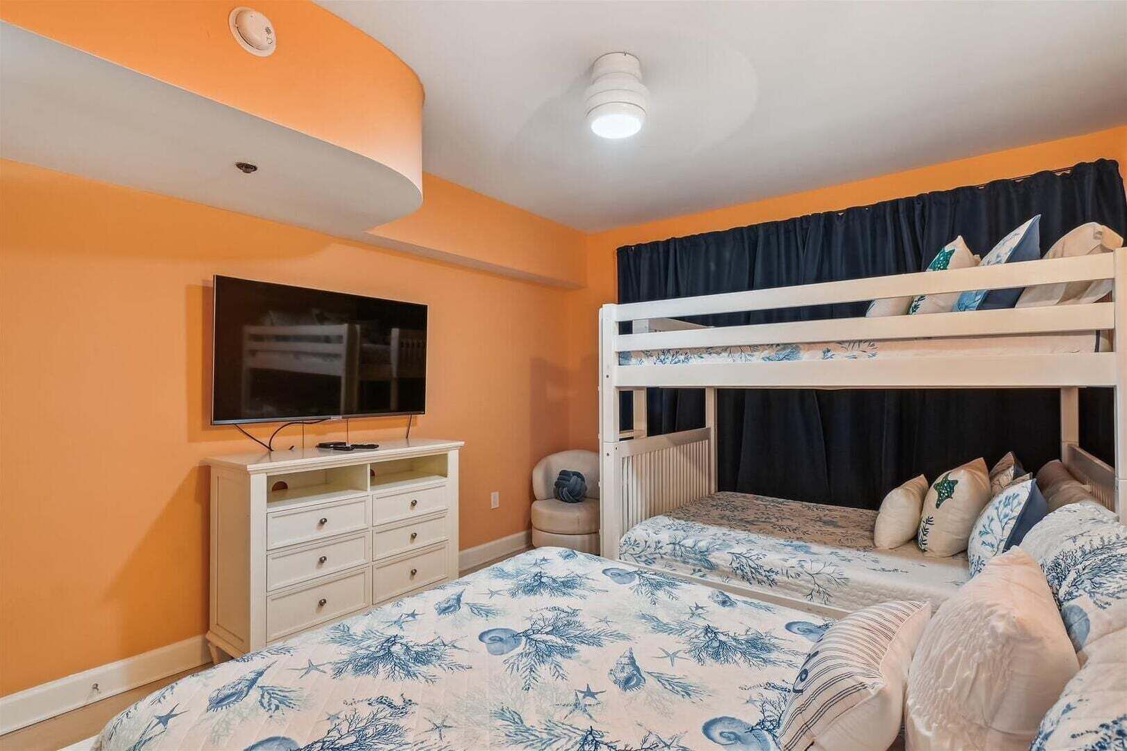 A room with a bunk bed, a television, a dresser, and a window with curtains.
