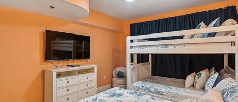 A room with a bunk bed, a television, a dresser, and a window with curtains.