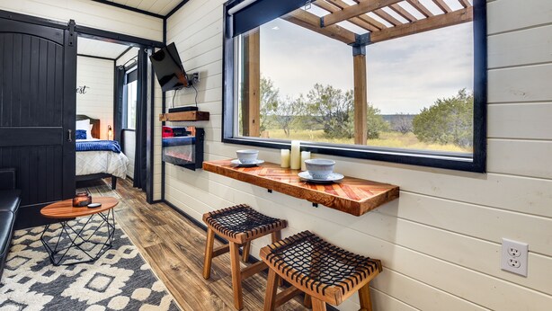 A cozy interior with a wooden bench, a small table, and a window overlooking a natural landscape. - Remote Strawn Container Home w/ Hot Tub! (Strawn)
