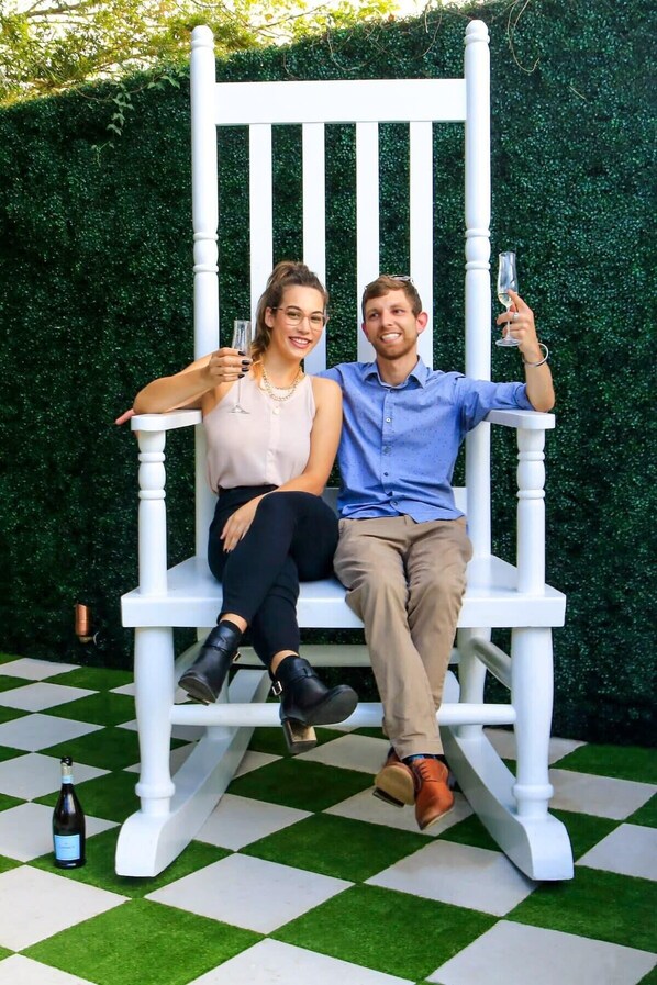 Two people sitting on a white chair with a green hedge in the background.