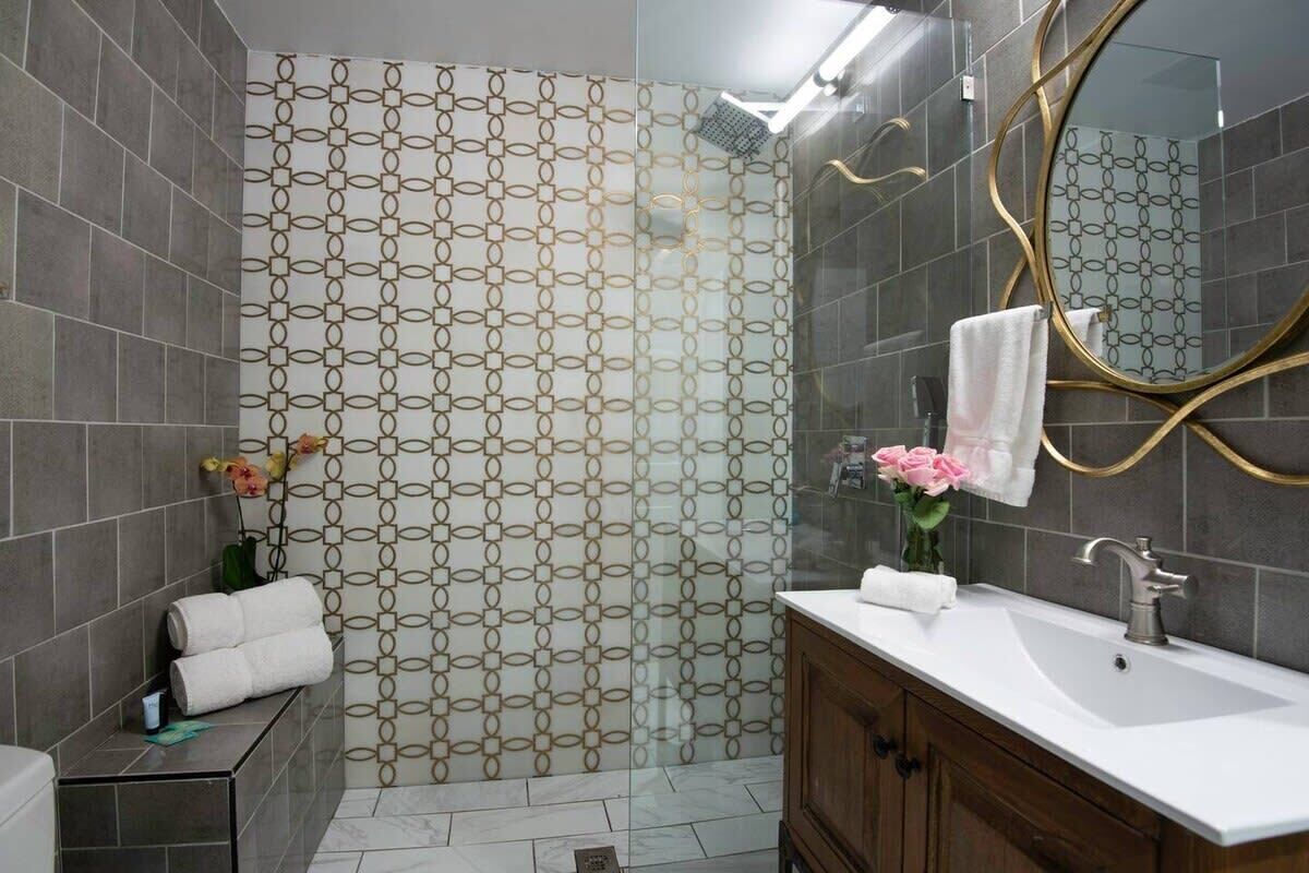 A modern bathroom with a patterned shower wall, a vanity with a mirror, and a towel rack.
