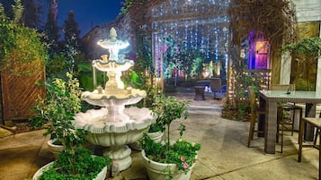 A garden with a central fountain, potted plants, and a dining area with tables and chairs.