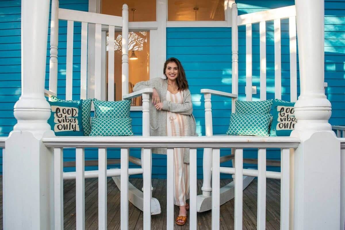A porch with a person standing, white railings, and patterned cushions with text.