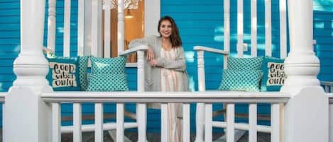 A porch with a person standing, white railings, and patterned cushions with text.
