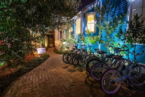 Een nachtzicht van een gebouw met een blauwe gevel, een met baksteen bestraat pad en verschillende fietsen die er geparkeerd staan.