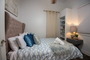 Une chambre à coucher avec une tête de lit capitonnée, une couvre-lit à motifs et une table de chevet avec une lampe.