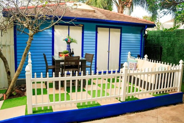 A blue house with white doors, a white picket fence, and a table with chairs outside.