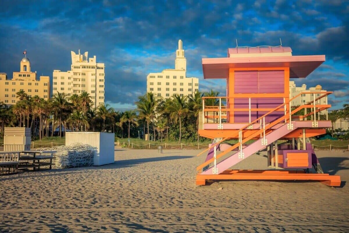 A lifeguard tower on a beach with palm trees and buildings in the background.