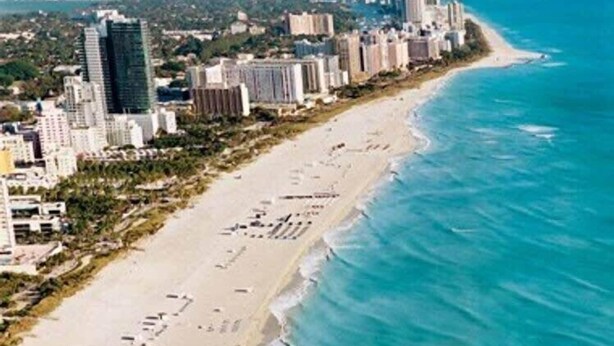 Paesaggio costiero con un'ampia spiaggia sabbiosa, grattacieli e un oceano blu cristallino.