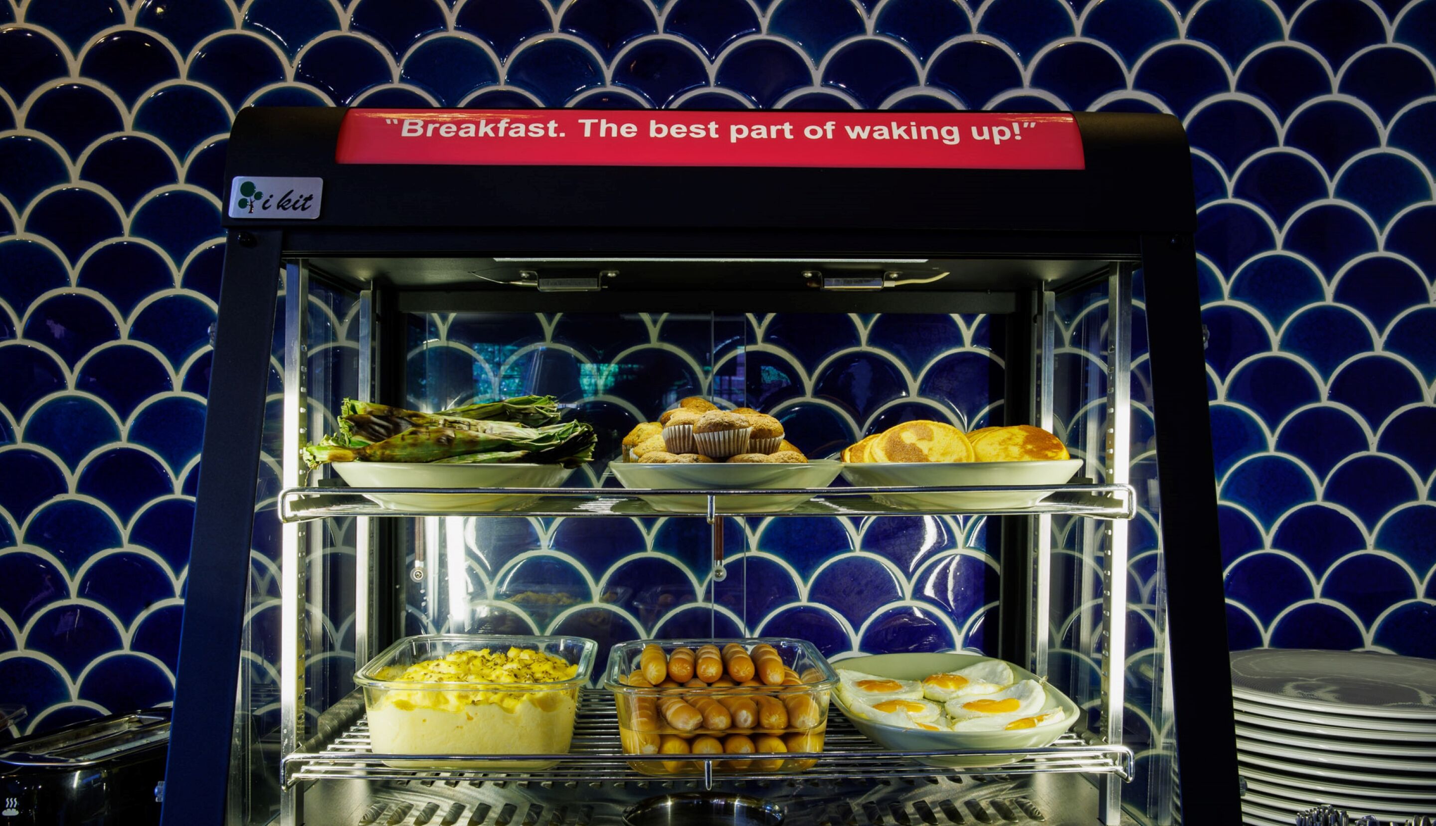 Vitrina de desayuno con diferentes opciones de comida, como panqueques, muffins y huevos.