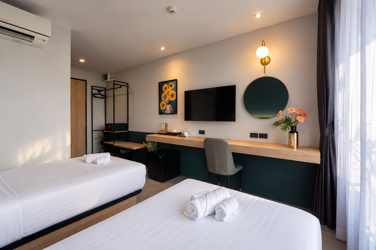 A hotel room with two beds, a desk, a chair, a TV, and a wall-mounted light fixture.
