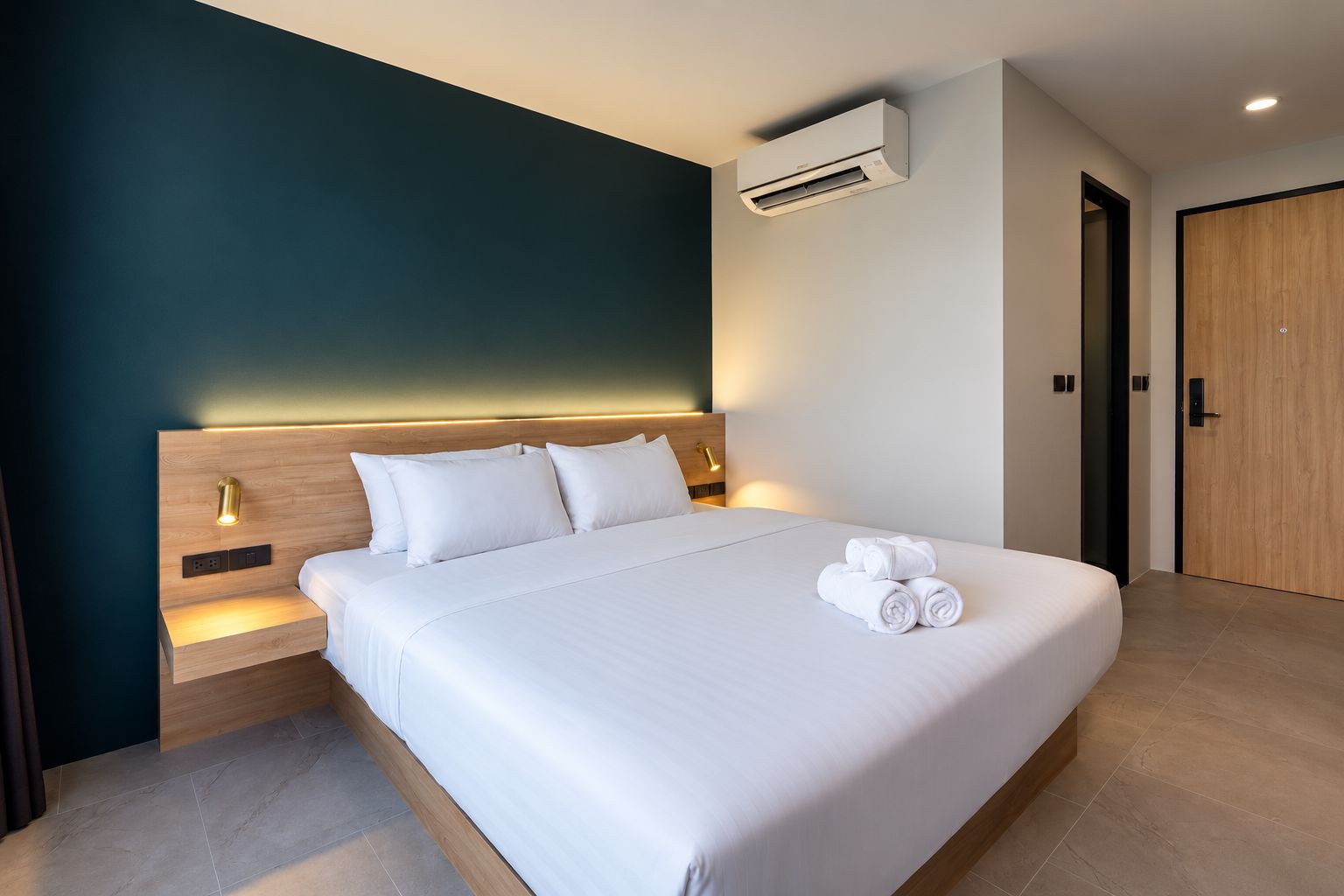 Ein Hotelzimmer mit einem großen Bett, einem Nachttisch, einer Klimaanlage und einer Holztür.