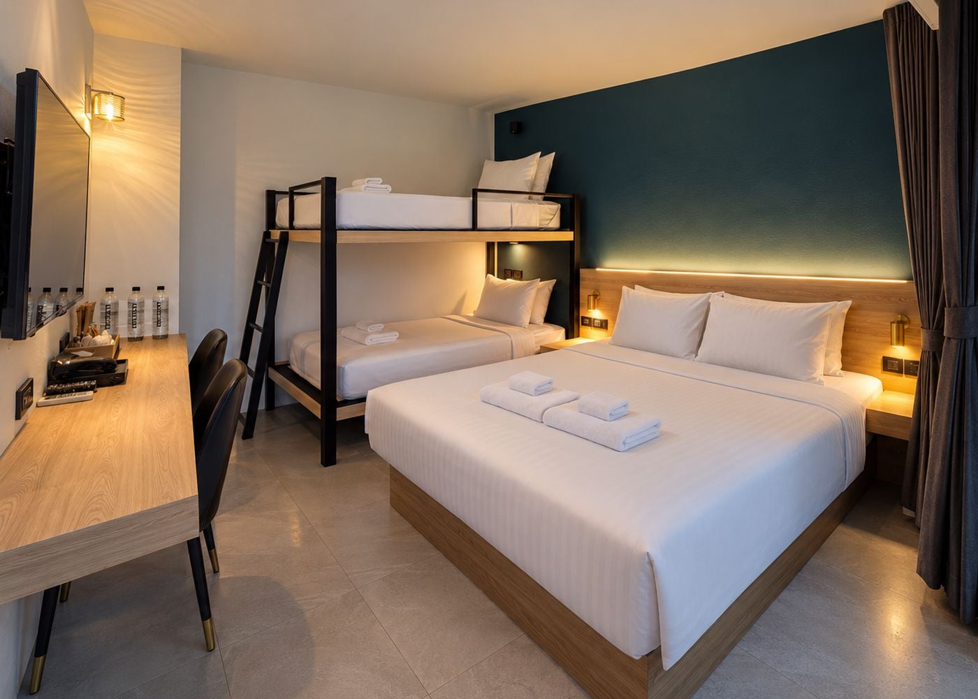 A hotel room with a bunk bed, a desk with a chair, and a bedside table with lamps.