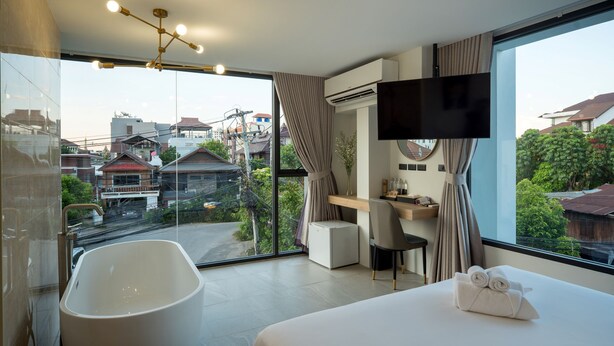 Ein modernes Hotelzimmer mit einem großen Bett, einer Badewanne, einem Schreibtisch mit Stuhl, einem Fernseher und Blick auf die Stadt.