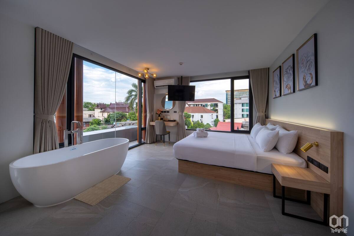 A modern hotel room with a large bathtub, a sofa bed, a desk, and a TV.