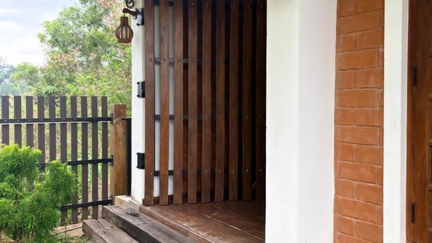 A wooden door with a vertical panel design, a small porch with a metal roof, and a brick wall. - Windy Hanthana (Kandy)
