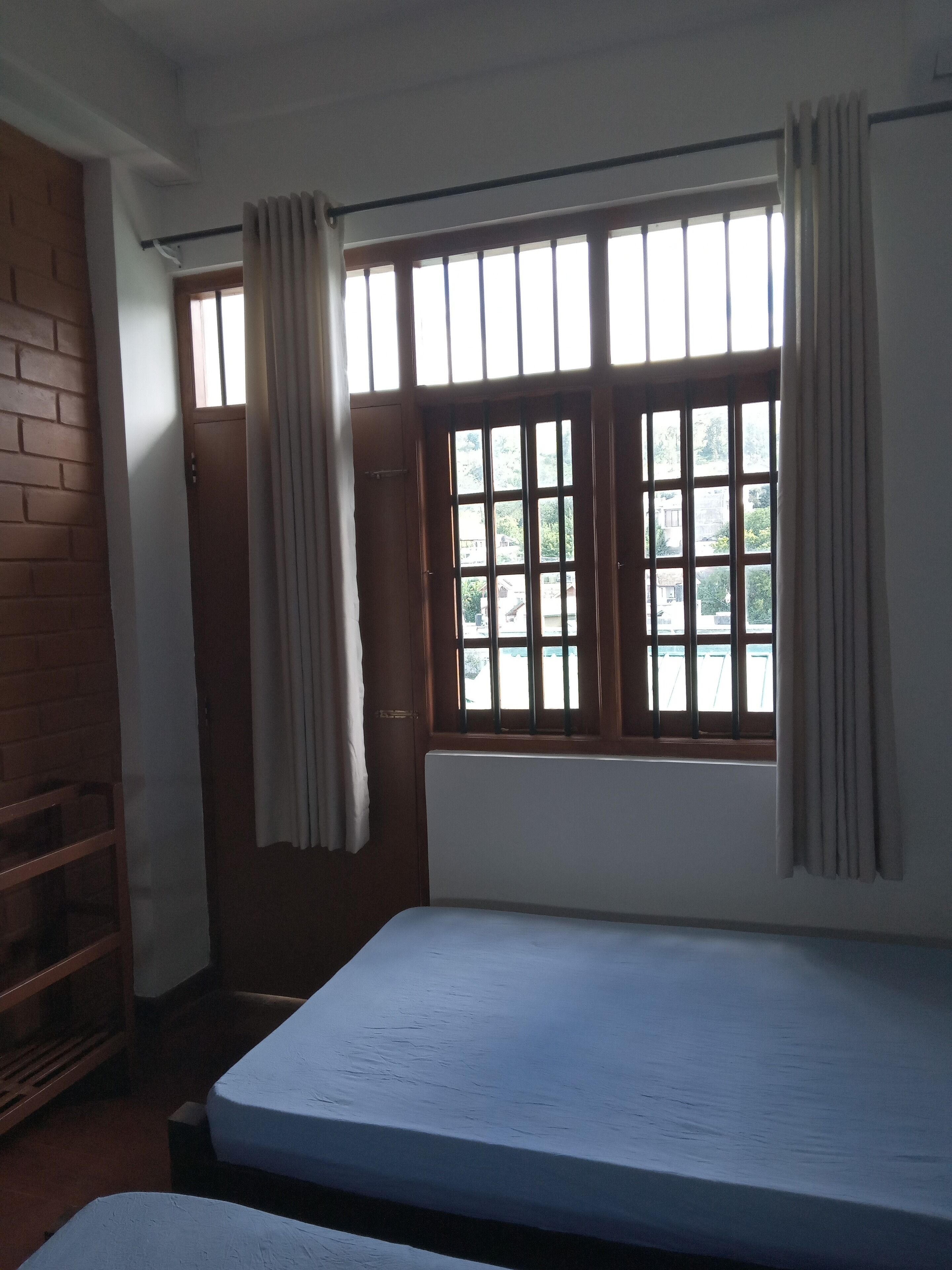 A room with a single bed, a window with bars, and a view of the outside.
