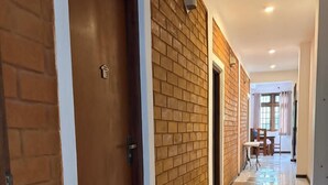 A hallway with a wooden door, a brick wall, and a tiled floor. - Windy Hanthana (Kandy)