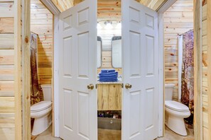 Ein Badezimmer einer Holzhütte mit zwei Toiletten, einem Duschbereich und einem kleinen Ablagekorpus.