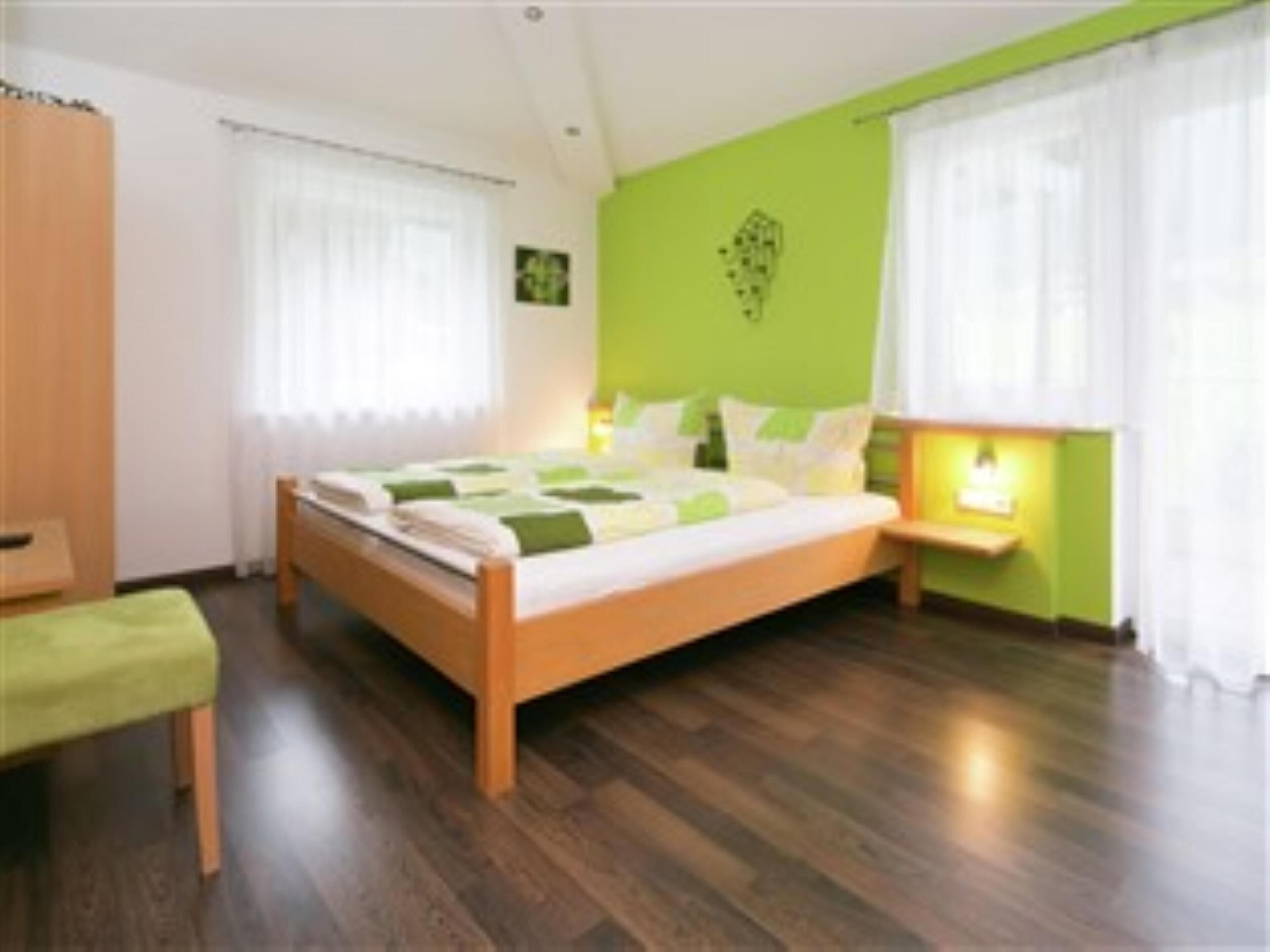A bedroom with a wooden bed, green walls, and a nightstand with a lamp.