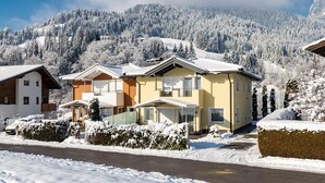 A snow-covered residential area with houses, a road, and a mountain in the background. - Beautiful group accommodation with sauna & ski-in (Itter)