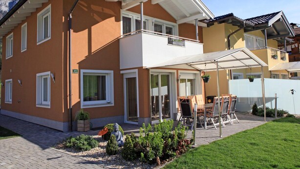 A two-story house with a balcony, a covered patio, and a small garden area. - Beautiful group accommodation with sauna & ski-in (Itter)