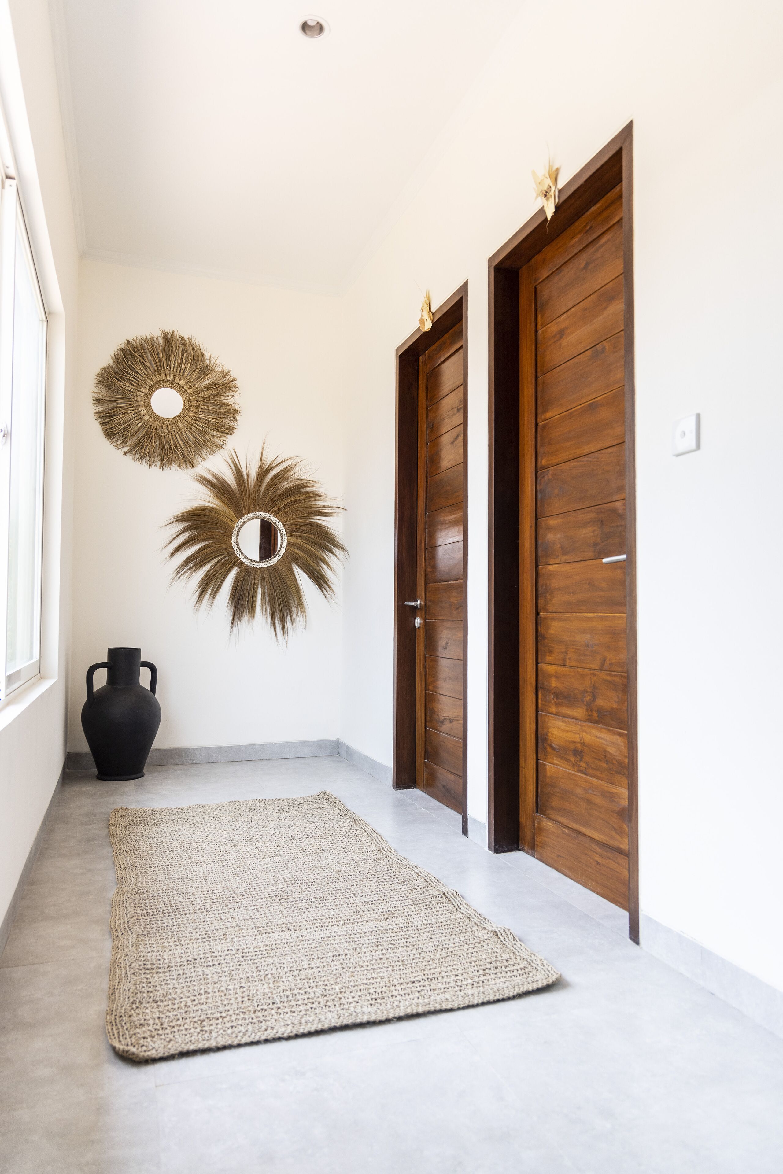 A hallway with a woven rug, two wooden doors, and wall-mounted decor.