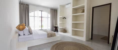 A modern bedroom with a built-in bench, a large woven rug, and a minimalist shelving unit.