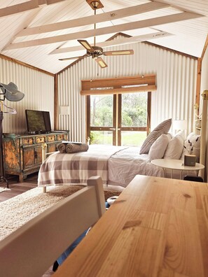 Een slaapkamer met een bed, een bureau, een stoel, een plafondventilator en een raam.