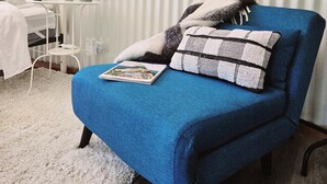Une pièce avec un fauteuil bleu, un lit blanc et un mur sur lequel est fixé un radiateur blanc.