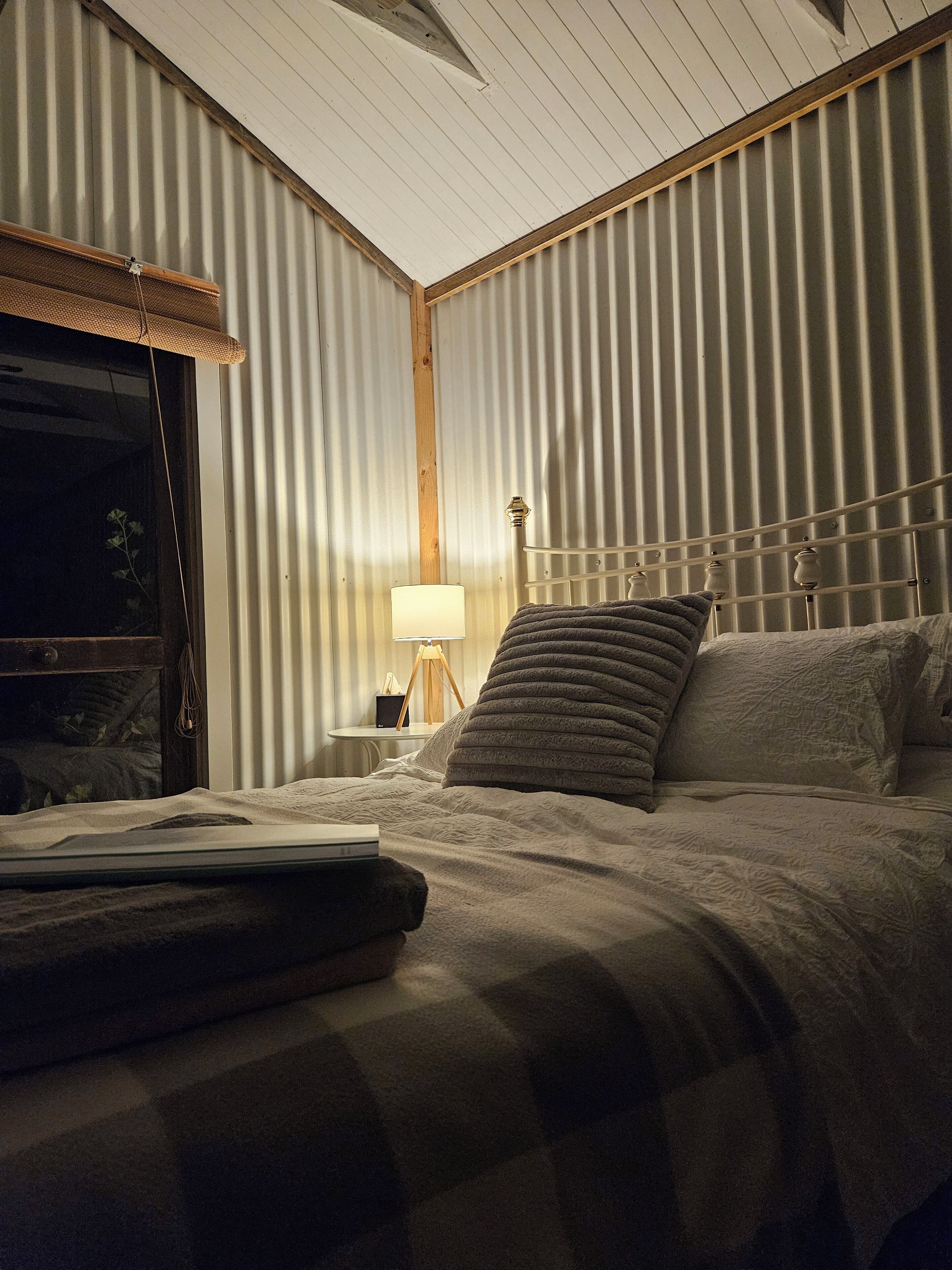 Une chambre à coucher avec un lit, une lampe de chevet, une table de chevet et une fenêtre avec des stores.