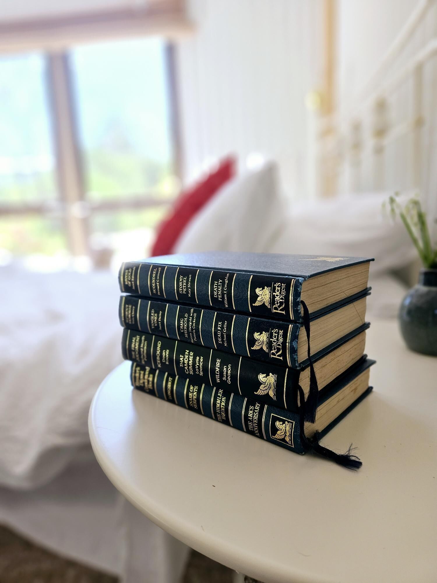 Una pila de libros sobre una mesa blanca en una habitación con una cama y una ventana.