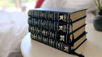Una pila de libros sobre una mesa blanca en una habitación con una cama y una ventana.