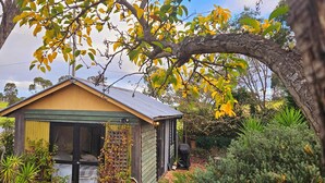 Une petite maison en bois d’un seul étage, avec un toit en pente, une véranda et une cour clôturée.