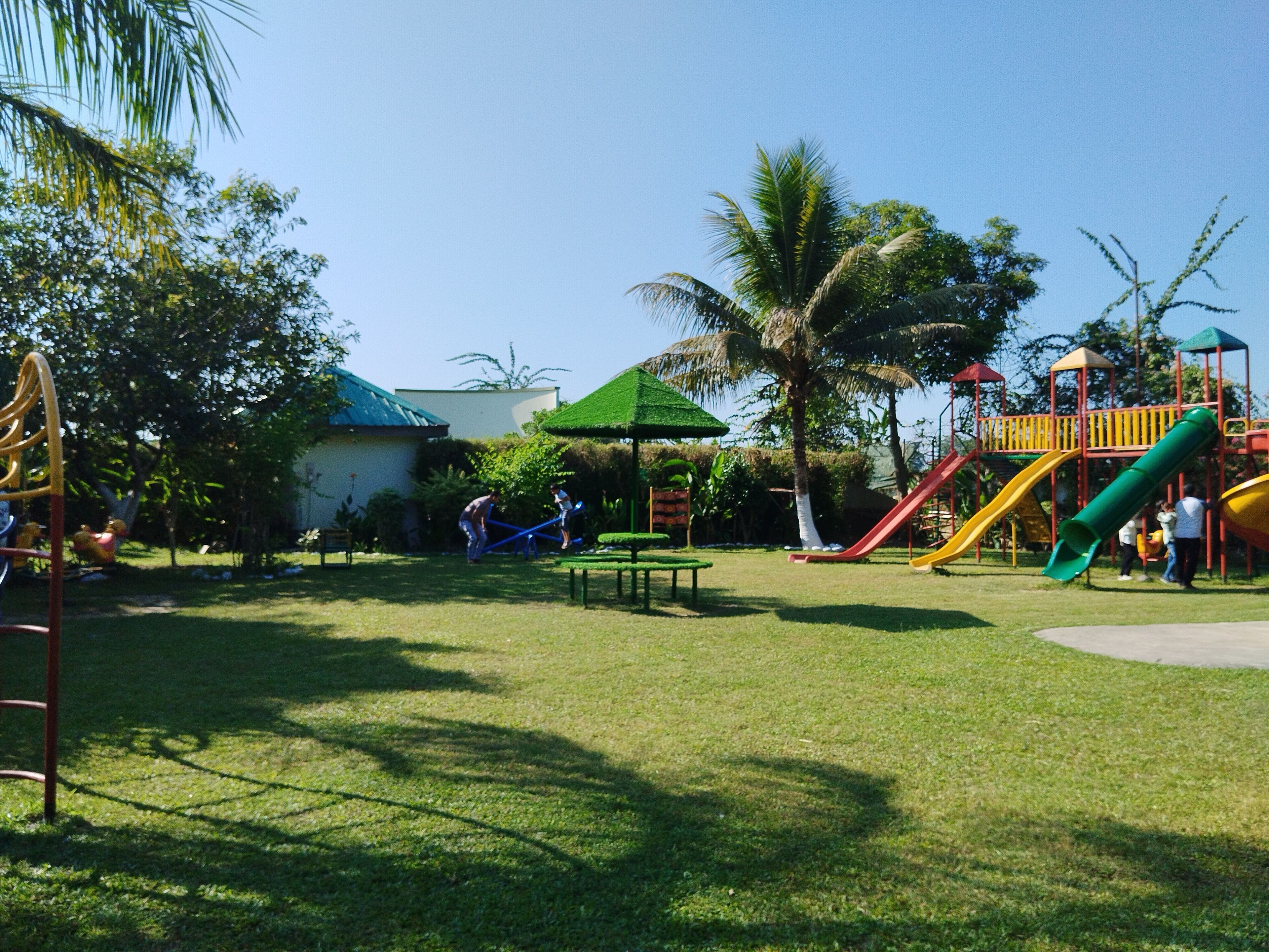 A playground with slides and climbing structures, surrounded by grass and trees.