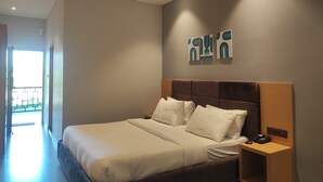 A modern hotel room with a large bed, a bedside table with a phone, and a wall-mounted artwork. - Padmini Resorts (Tinsukia)
