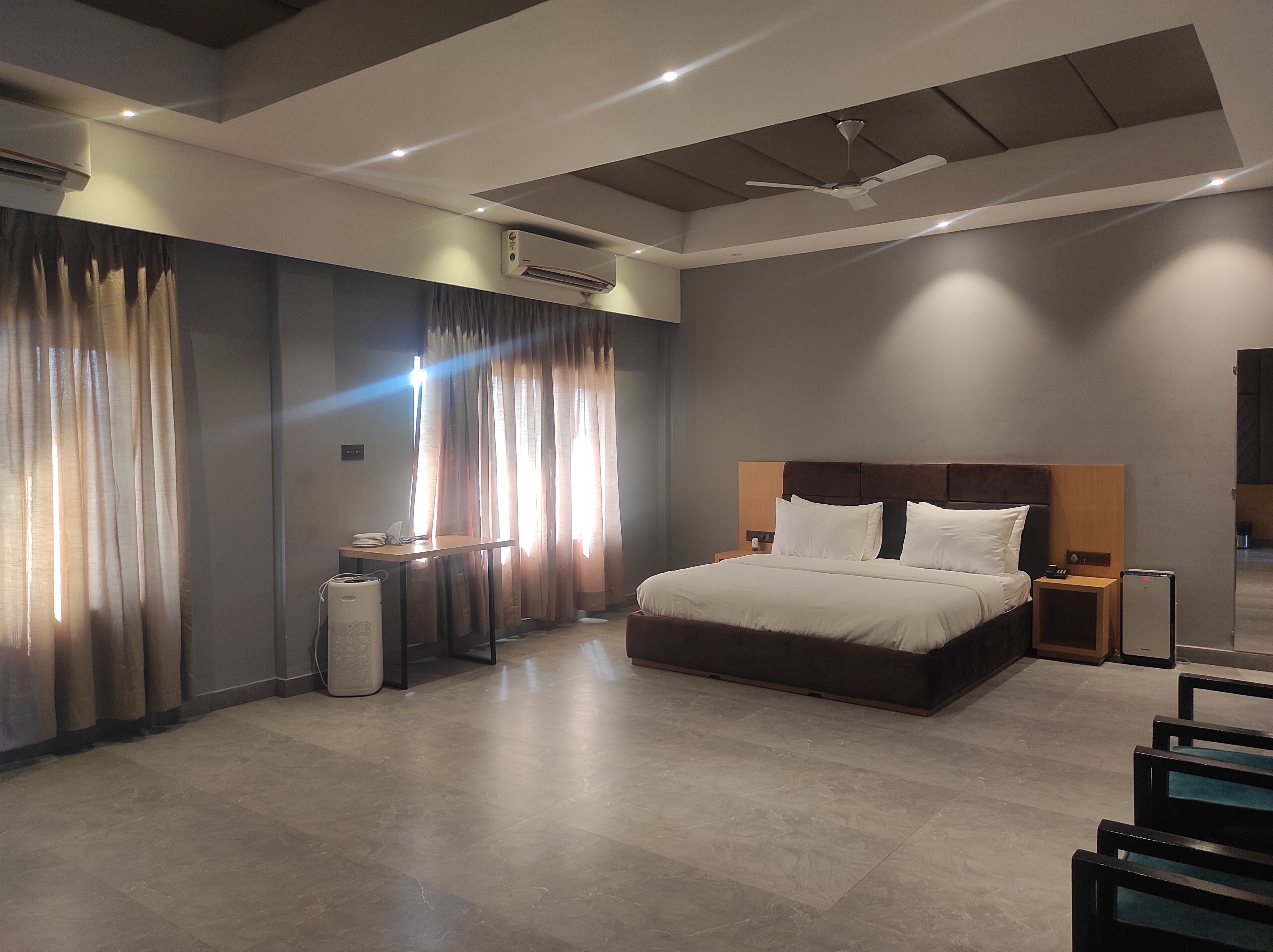 Una habitación de hotel moderna con una cama grande, una mesita de noche y un ventilador de techo, además de aire acondicionado.