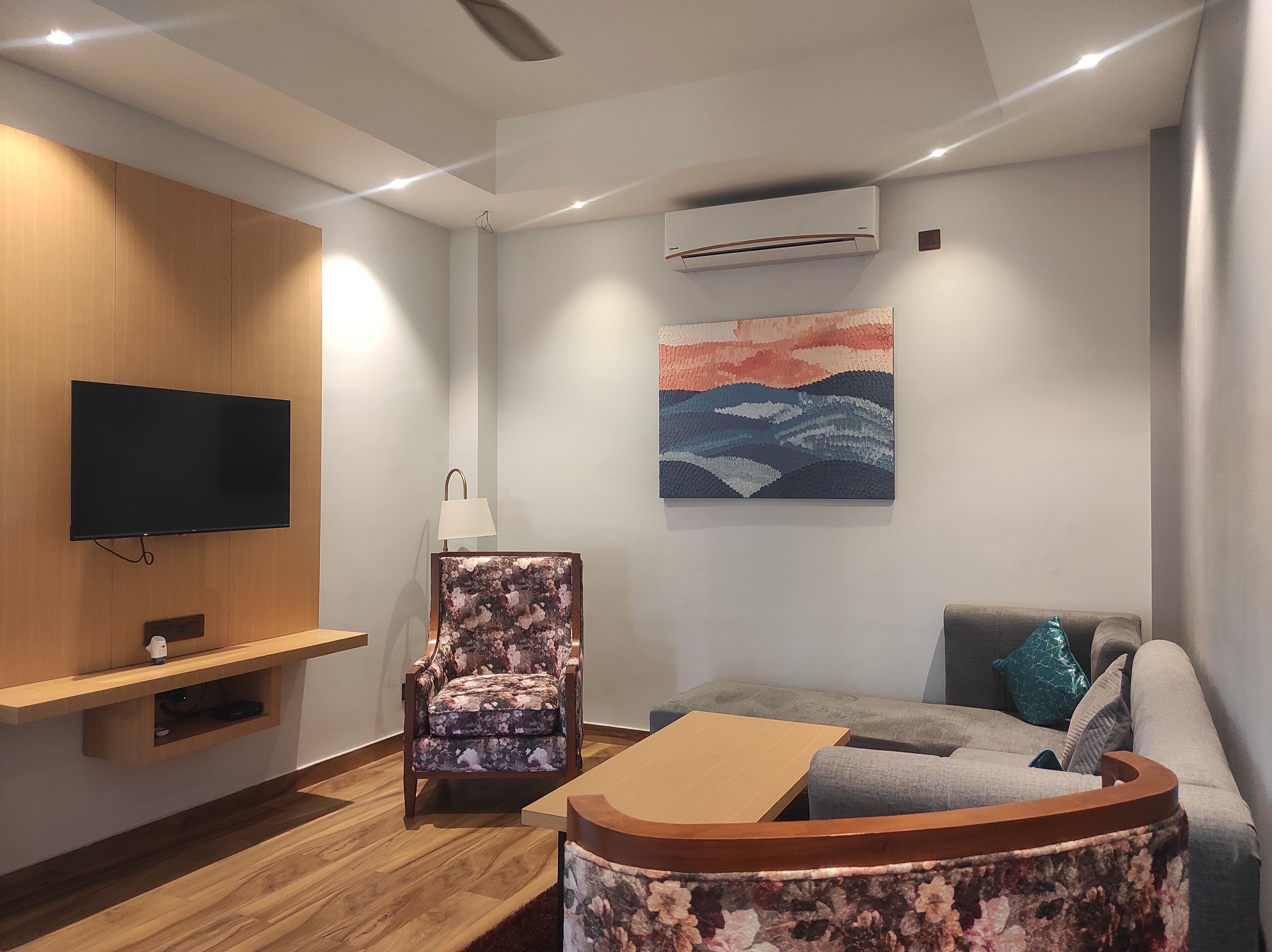 Una sala moderna con un televisor de pantalla plana, un sillón estampado, un sofá gris y una mesa de centro de madera.
