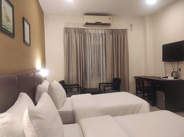 A hotel room with two beds, a desk, a chair, a television, and an air conditioning unit. - Padmini Resorts (Tinsukia)