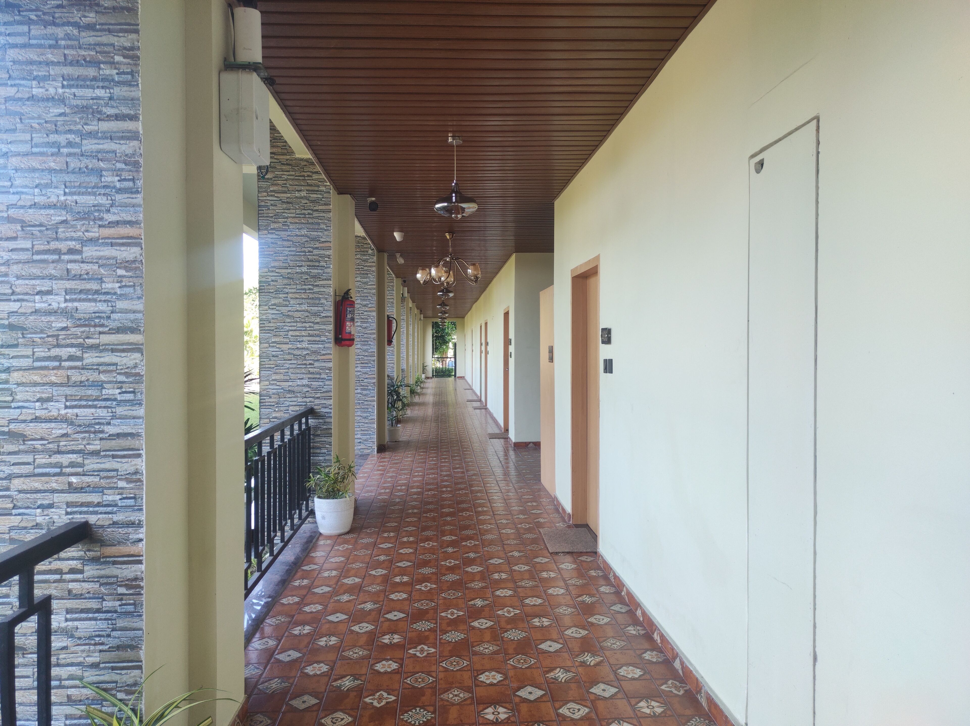 A corridor with patterned floor tiles, a stone wall on one side, and doors on the other.