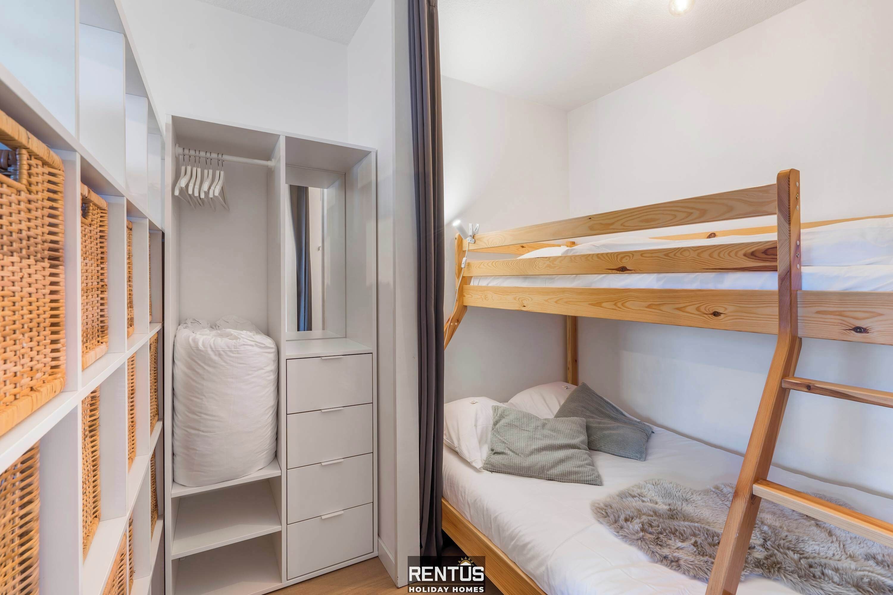 Ein Stockbett mit Holzrahmen und weißer Bettwäsche, ein weißer Kleiderschrank mit Kleiderstange und ein flauschiger Teppich auf dem Boden.