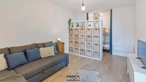 A modern living room with a grey sofa, a white TV stand, and a wall unit with baskets. - Sandy View - spacious studio flat near the beach (Nieuwpoort)