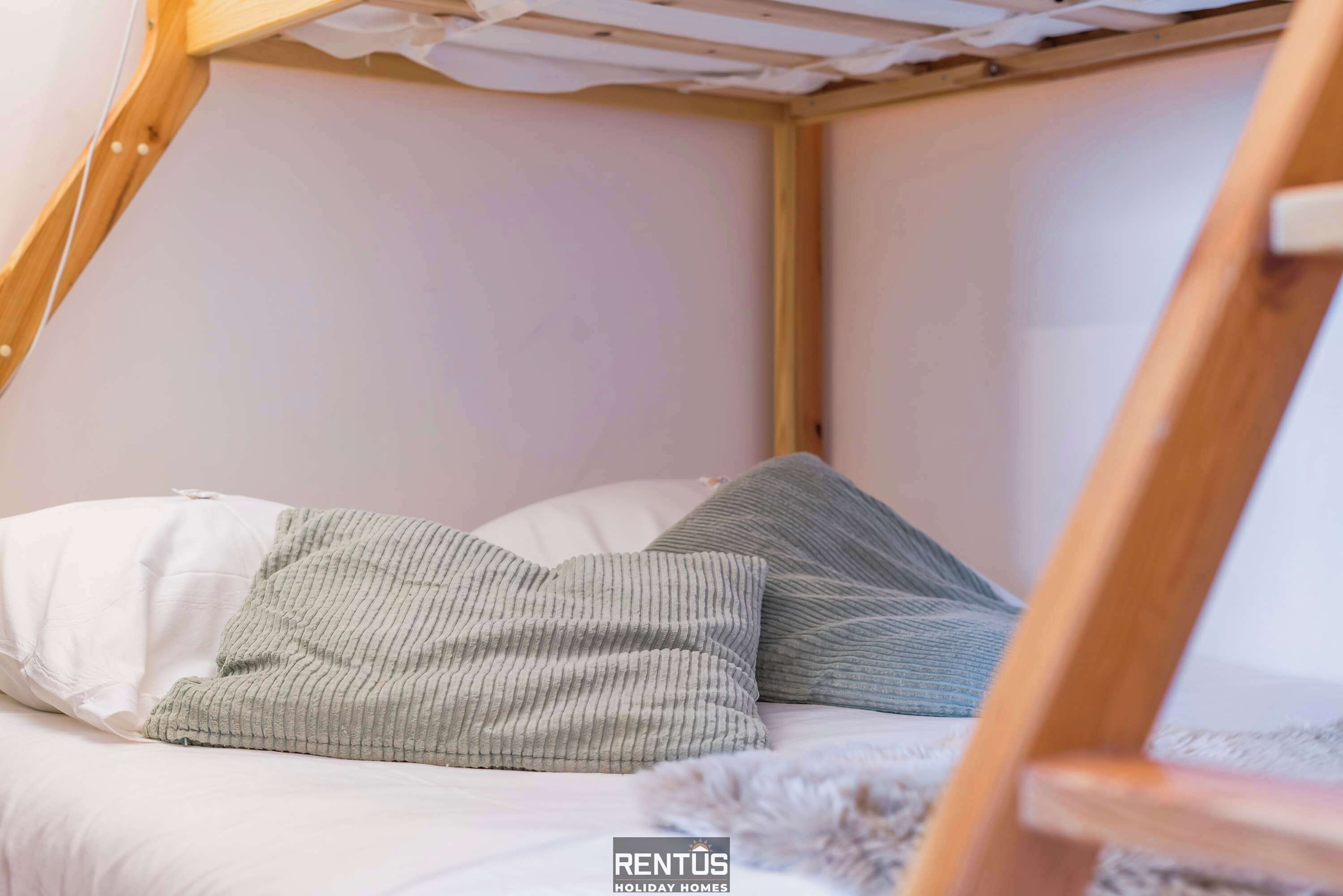 Une chambre mansardée chaleureuse, avec un plafond en pente, un lit agrémenté d’oreillers à rayures blanches et vertes, et une chaise en bois.